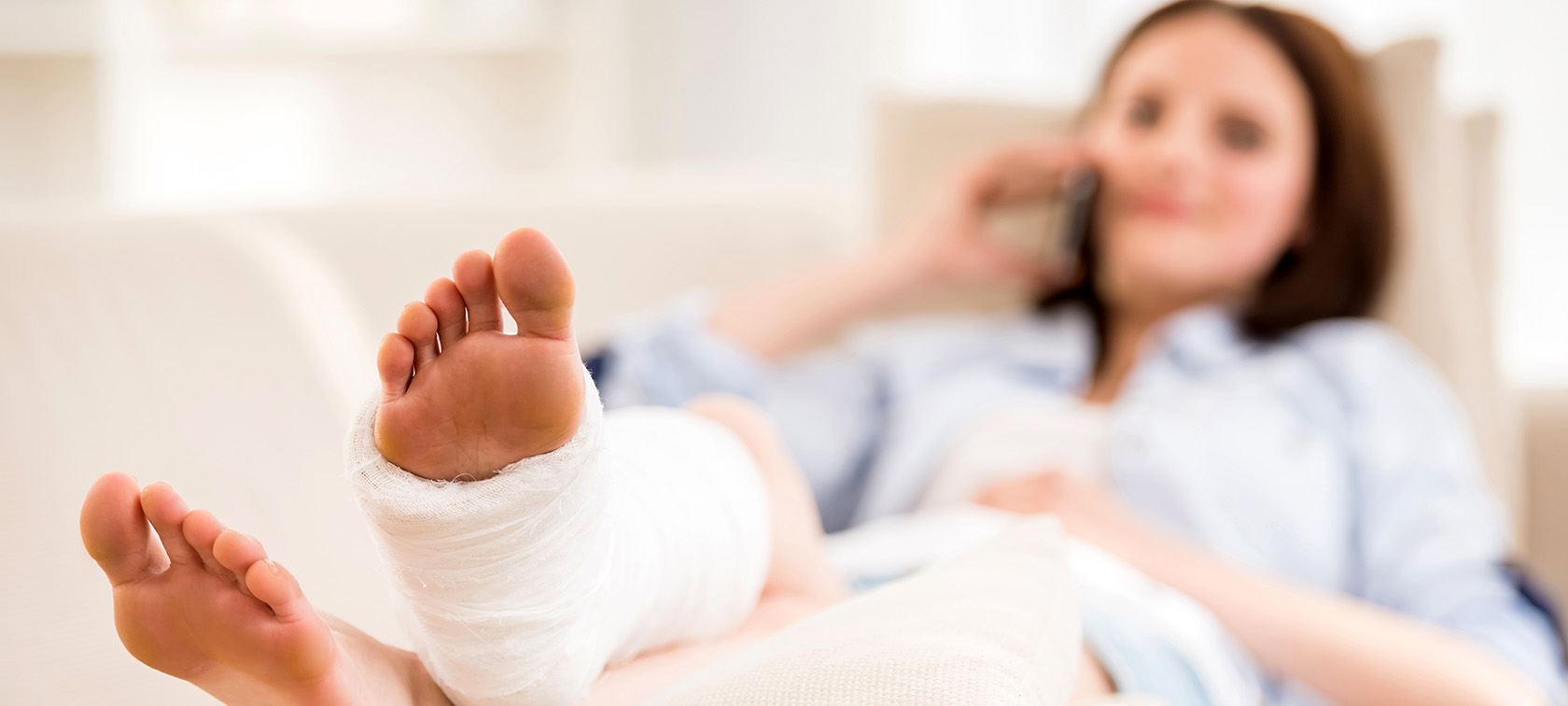 Frau liegt mit eingegipsten Fuß auf einem Sofa und telefoniert Frau liegt mit eingegipsten Fuß auf einem Sofa und telefoniert.
